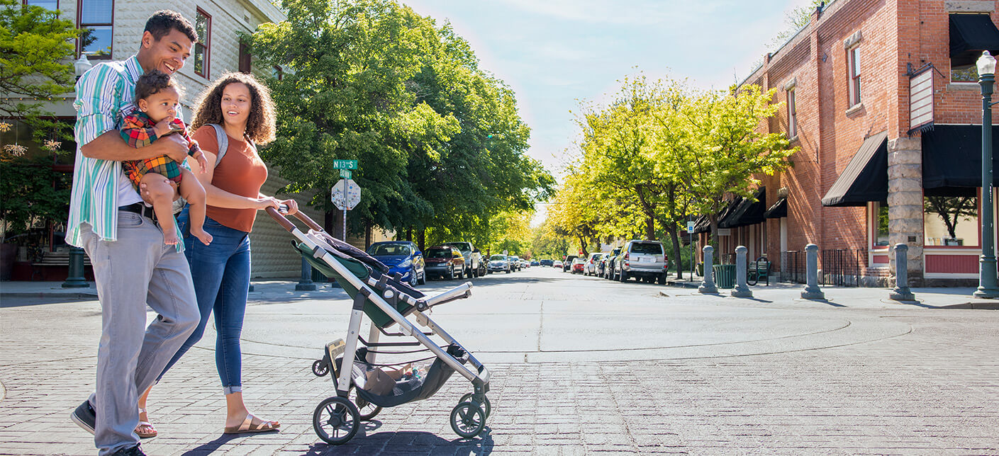 Couple holding their baby while pushing the stroller across a street